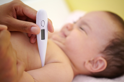 Un nadó plorant al bressol amb un termòmetre sota el braç