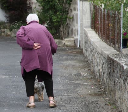 Una senyora gran d'esquenes camina pel carrer amb dificultat.