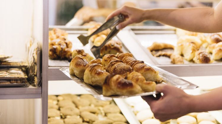 Unes mans sostenen una safata de croissants petits darrere el mostrador d'un forn