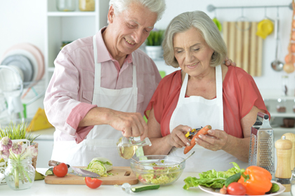 Una parella de persones grans prepara una amanida a la cuina
