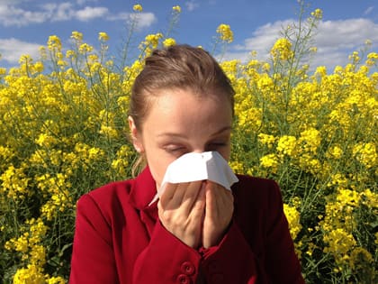 Una noia es tapa el nas i la boca amb un mocador enmig d'un camp ple de flors
