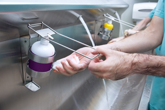 Les mans d'un professional sanitari sota un dosificador de sabó