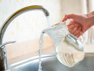 Una mà subjecta una gerra d'aigua que vessa sota el raig d'una aixeta 