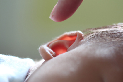 Pla detall d'un dit que s'acosta a l'orella d'un nadó estirat de costat