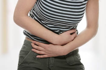 Una noia amb l'esquena doblegada es toca l'abdomen amb les dues mans en senyal de dolor