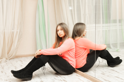 Una noia asseguda d'esquenes a un mirall