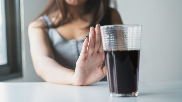 Una noia fa un gest de rebuig amb la mà davant d'un got amb refresc de cola