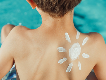 Un infant d'esquenes amb un sol dibuixat amb crema de protecció solar