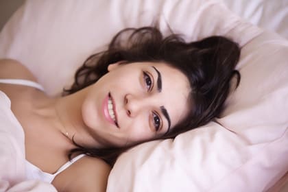 Una noia que s'acaba de despertar somriu estirada al llit